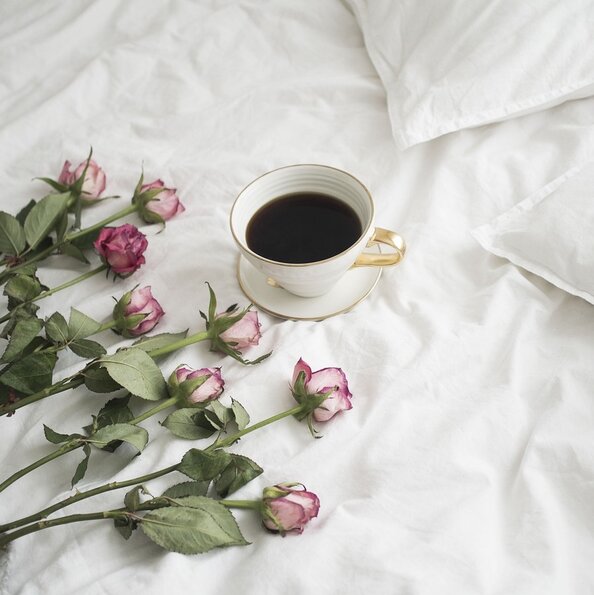 Eine Tasse Kaffe und Rosen auf weißer Bettdecke